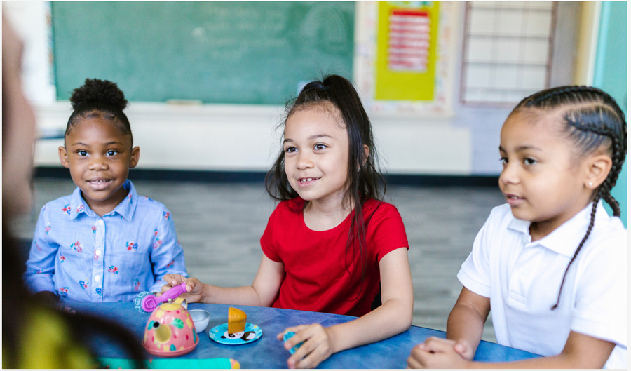 three young children smiling in a classroom around a table